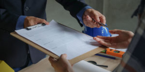 Close up of person in suit handing a document and pen to another person.