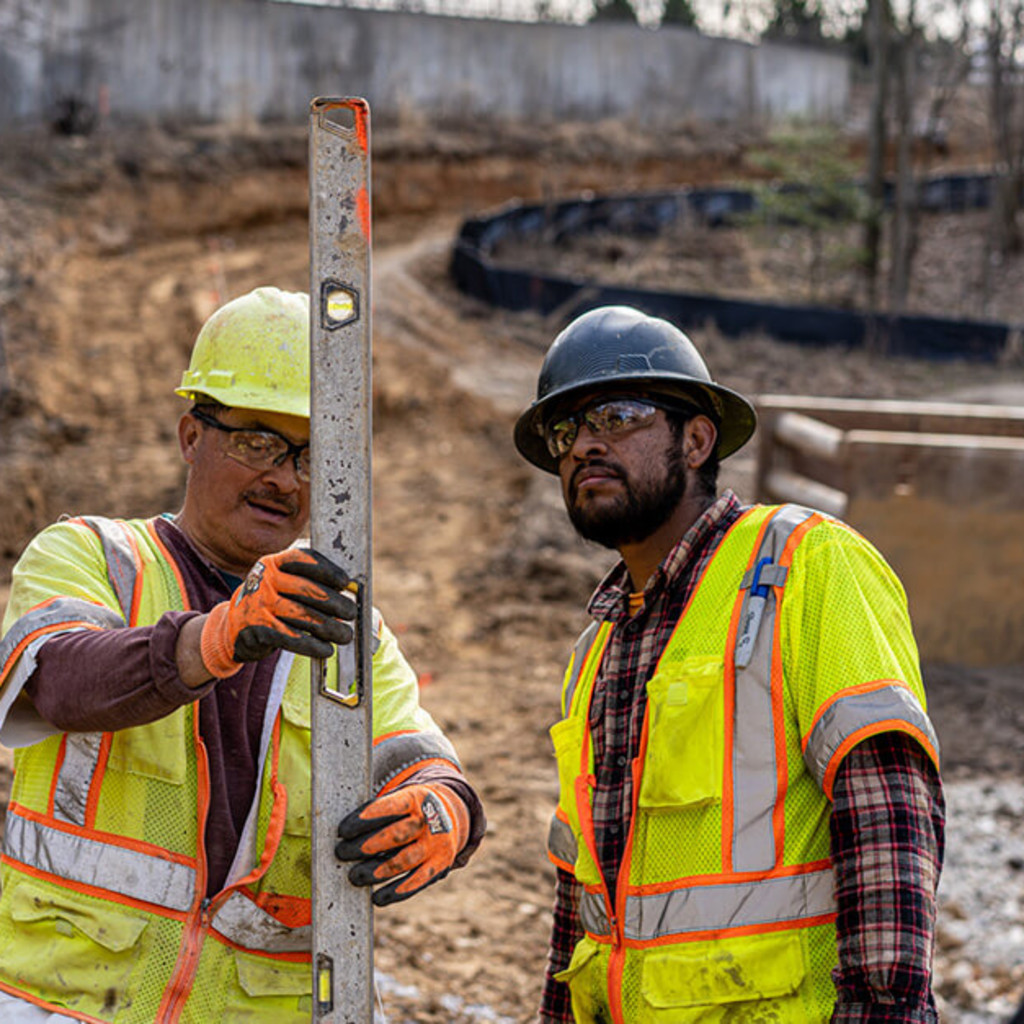 Two construction workers wearing safety vests and helmets holding a level on site